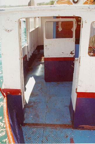 Photo 11 - Opening in bridge front with stove-in door forced inside superstructure and unpainted, corroded foot print on main deck of missing door sill